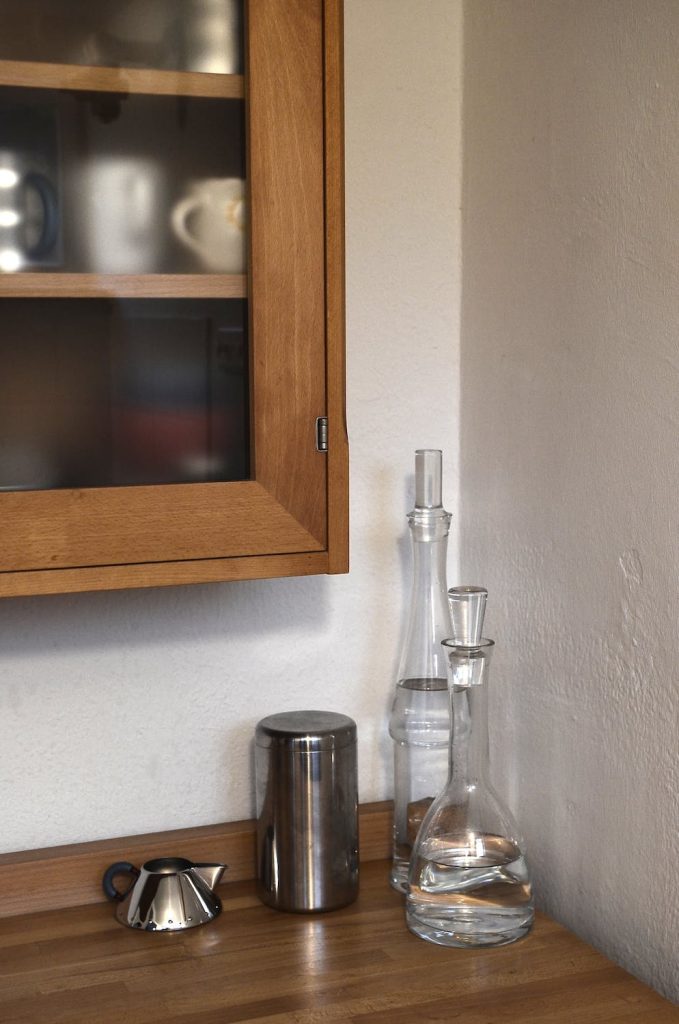 Cupboard with cups above counter with bottles and pot